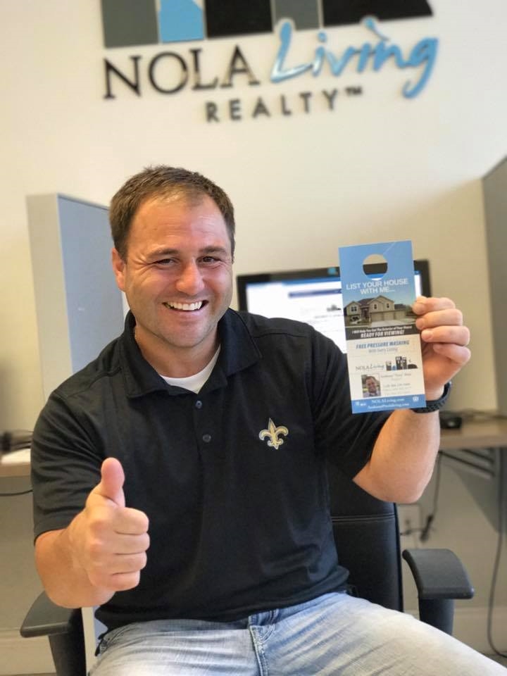Agent Tony Ruiz proudly poses with a custom door hanger, designed by NOLA Living's in-house graphic designer and marketing manager. All NOLA Living agents have the designer at their disposal to create custom marketing pieces, both for print and web.