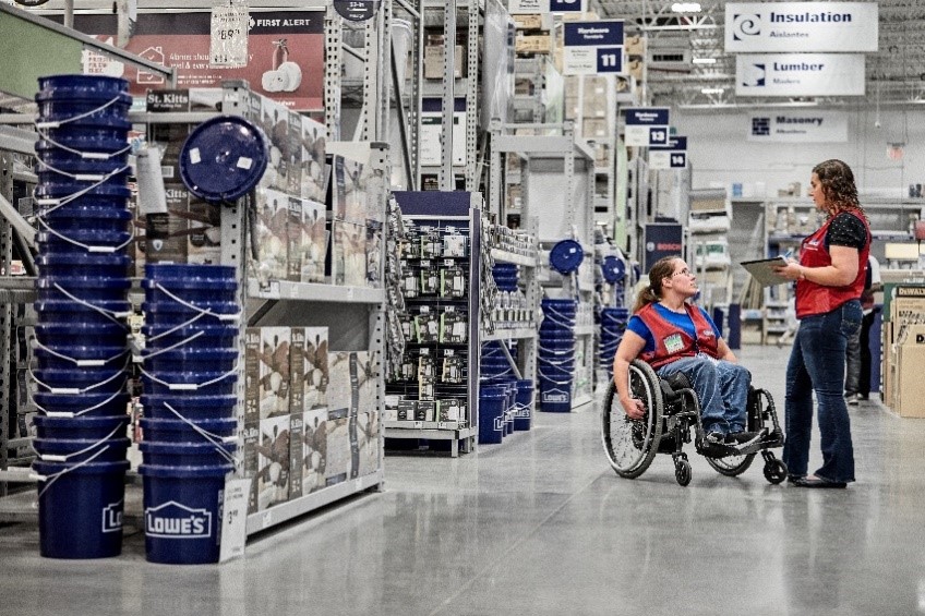 Two Lowe's associates wearing red vests, one in a wheelchair talking to each other.