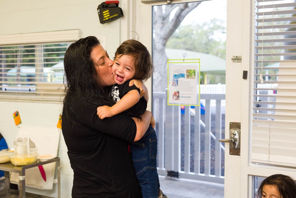 A mother says goodbye to her child inside of his classroom before heading to work