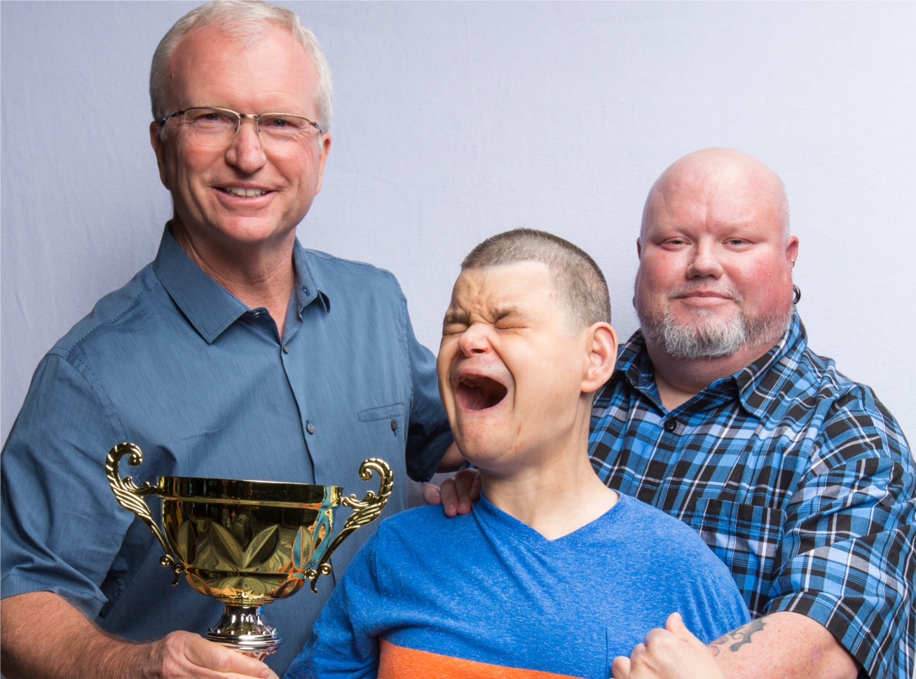 Brad, HGH Resident, happily receives the 2019 Client of the Year Award. At his sides are donor, Dave Walker (left) of Avista Technologies and Brad's caregiver and buddy, Derek.