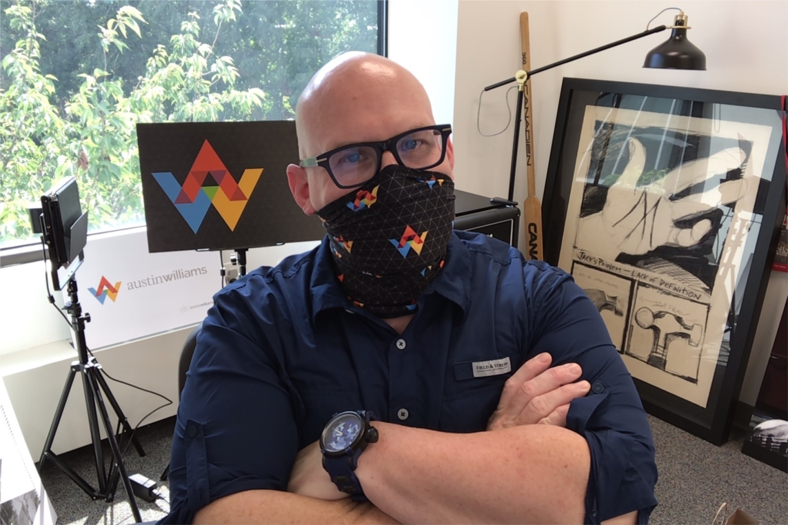 Austin Williams Creative Director Bryan Hynes in his office, wearing an AW-branded gaiter face covering he helped design for employees to return to the office.
